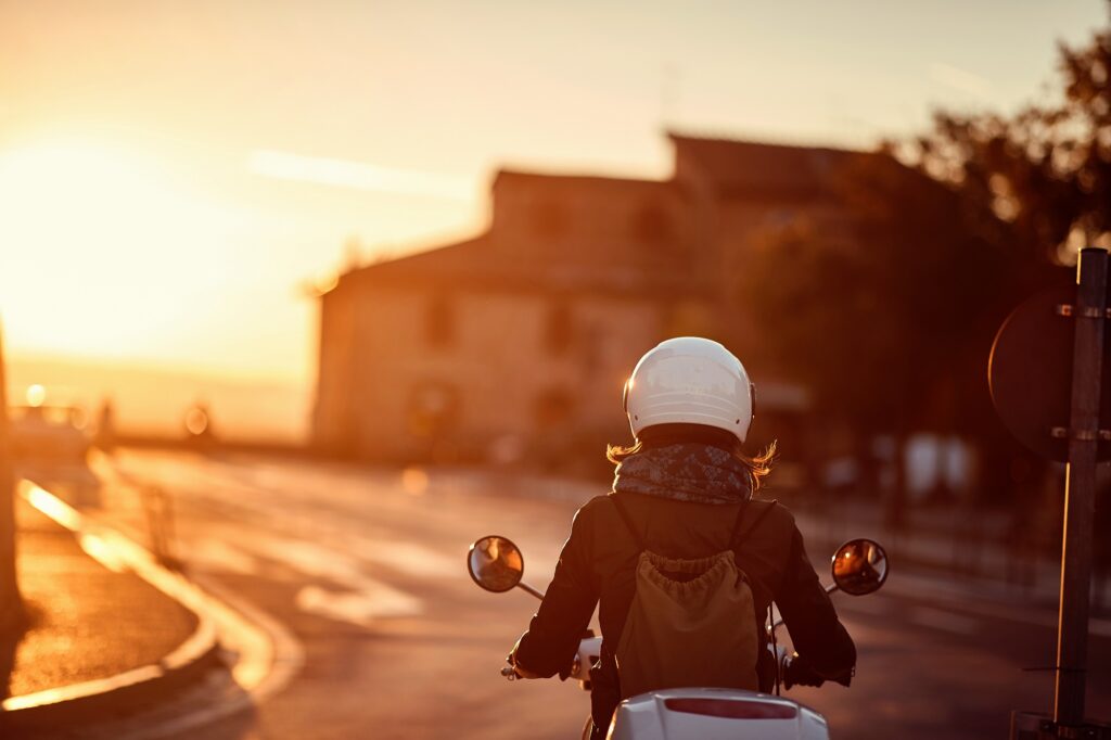Young woman riding moped on road into sunset
