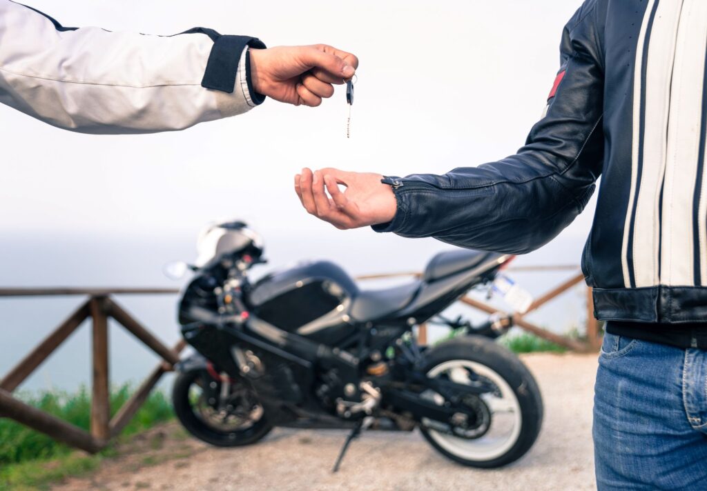 Two people exchanging keys with motorcycle in the background